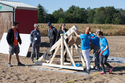 group of people stand around a trebuchet
